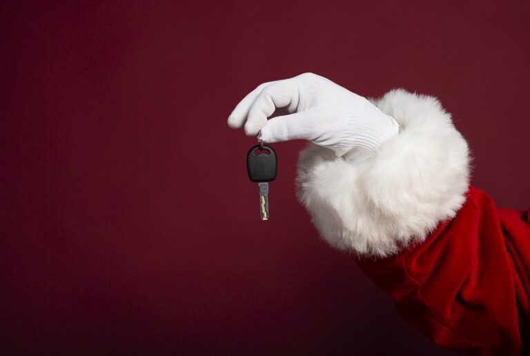 Male hand in white glove and Santa Clause costume holding key on red background, Christmas and New year concept